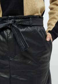 Zwarte leren rok met een gestructureerde afwerking, voorzien van een aansluitende taille en een bijpassende strikriem. Inclusief zijzakken voor functionaliteit.