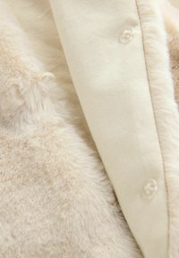 Gros plan sur un tissu en fausse fourrure beige à côté d'un tissu lisse crème avec des boutons en plastique transparent cousus.
