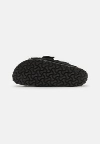 Black slipper with a textured rubber sole featuring a wave pattern. The upper material appears soft, with a Velcro strap for closure.