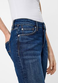 Džínové kalhoty v tmavě modré barvě s přiléhavým střihem. Mezi vlastnosti patří přední kapsy, viditelné švy, logo štítek a hladká textura.