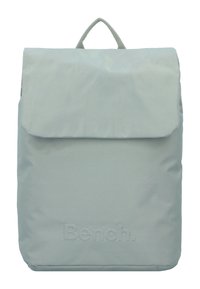 Light blue backpack with a flap closure and top handle. Made of smooth fabric with embossed logo detail at the bottom. Simple, rectangular shape.