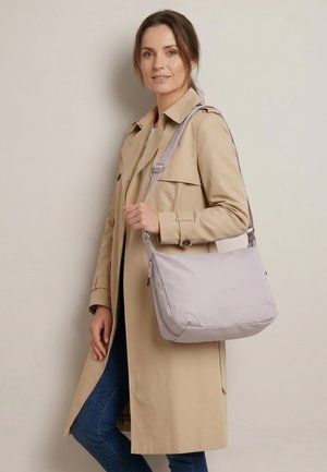 Kvinde iført beige trenchcoat og blå jeans, bærer en lysegrå skuldertaske med justerbar rem.