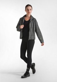 Grå och svart rutigt jacka med krage, i kombination med en svart topp och leggings. Svarta skor och mönstrade strumpor kompletterar looken.