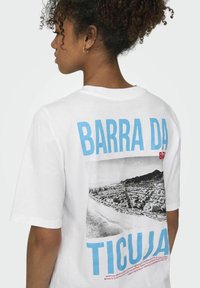 Witte katoenen t-shirt met een grafisch ontwerp op de achterkant. De tekst "BARDA DA TICUJA" staat in blauw en rood, met daaronder een zwart-wit afbeelding.