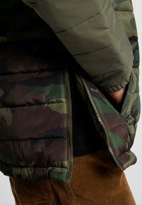 Polstret jakke i grøn og brun camouflagemønster med lynlåslukning, ribbet manchetter og elastisk linning.