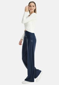 Navy wide-leg pants made of smooth fabric with a high waistband, paired with a long-sleeve white top. Notable pocket accents.