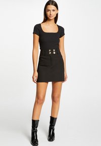 Black ribbed top with short sleeves and square neckline, paired with a high-waisted black skirt featuring gold-button accents and side pockets.