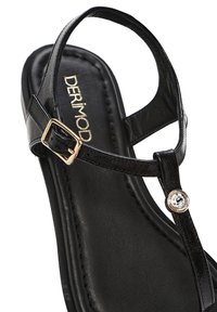 Sandal con tacco nero con finitura lucida, cinturino alla caviglia, fibbia color oro e un accento decorativo di strass sulla fascia della punta.