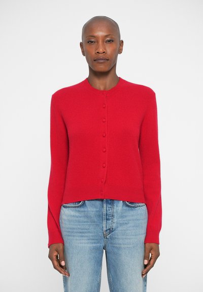 Cardigan tricoté rouge avec un col rond, des manches longues et des boutons sur le devant. L'ourlet est légèrement raccourci, associé à un jeans bleu clair.