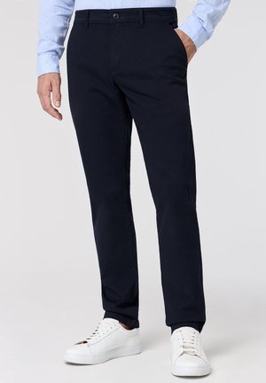 Marineblaue Chinos aus gewebter Baumwolle, mit einem geraden Schnitt, Seitentaschen und einem klassischen Knopfverschluss, getragen mit weißen Sneakern.