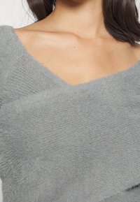 Grijs fuzzy sweater met een V-hals ontwerp, met een zachte textuur en overlappende stoflagen. Close-up van de halslijn en schoudergebied.