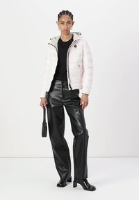 Giacca bianca imbottita con cappuccio grigio, chiusura con zip e tasche frontali, abbinata a pantaloni in finta pelle nera e stivaletti, accessoriata con una borsa piccola.