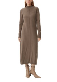 Langes, gestricktes, braunes Kleid mit hohem Kragen, gerippten Bündchen und gerader Silhouette. Tragen mit cremefarbenen Stiefeletten und neutralem Hintergrund.