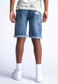 Leren denimshorts in lichtblauw met opgerolde manchetten; heeft twee achterzakken en een zijzak; gecombineerd met witte sneakers en sokken.