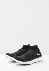 Chaussures de sport noires avec un dessus en maille tricotée, design de bande élastique et semelles en caoutchouc blanches. Logo Nike notable en blanc.
