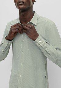 Groen geruit overhemd met knopen, een gestructureerde kraag, lange mouwen en parelmoeren knopen. Heeft een subtiele patroonstructuur.