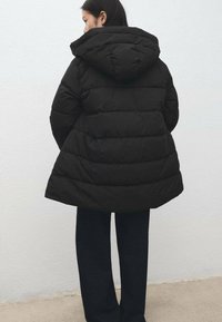 Czarna puchowa kurtka z kapturem, z pikowanym wzorem i długością do kolan. Gładka tekstura z lekkim połyskiem.