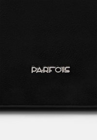 Superficie nera testurizzata con una piccola placca in metallo argentato con la scritta "PARFOIS" centrata vicino al bordo inferiore.