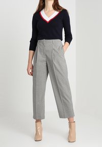 Jersey marino con escote en V rojo y blanco, combinado con pantalones de cuadros grises de cintura alta. La modelo lleva botas de tobillo beige.