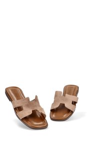 Sandalias deslizantes de ante beige con dos correas anchas, punta redondeada y suela marrón suave. Material texturizado y diseño minimalista.