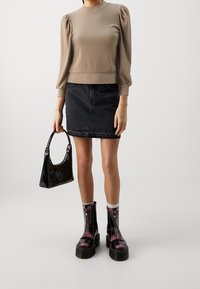 Maglione beige a costine con maniche a sbuffo, gonna di jeans nera, borsa in vernice nera, e stivali neri e viola con zip. Superfici piatte e strutturate.