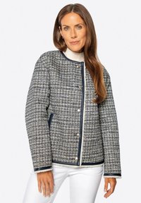 Steppjacke mit einem strukturierten, marineblauen und weißen Gewebemuster, silbernen Hardwareknöpfen und kontrastierendem marinen Besatz entlang der Kanten.