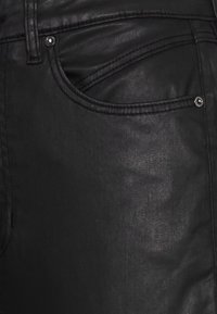 Black faux leather jeans with a smooth texture, featuring a front pocket, silver hardware, and subtle stitching details.