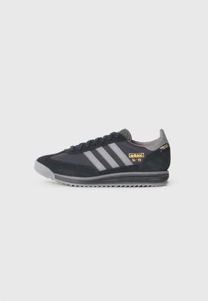 Sort og grå Adidas SL 72 sneaker med tre grå striber og gyldent logo på siden, grå sål og sorte snørebånd på hvid baggrund.