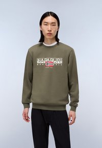 Oliven grøn sweatshirt med rund hals, prydet med et markant grafisk logo i hvid og rød. Lange ærmer og ribbede manchetter. Sorte bukser.