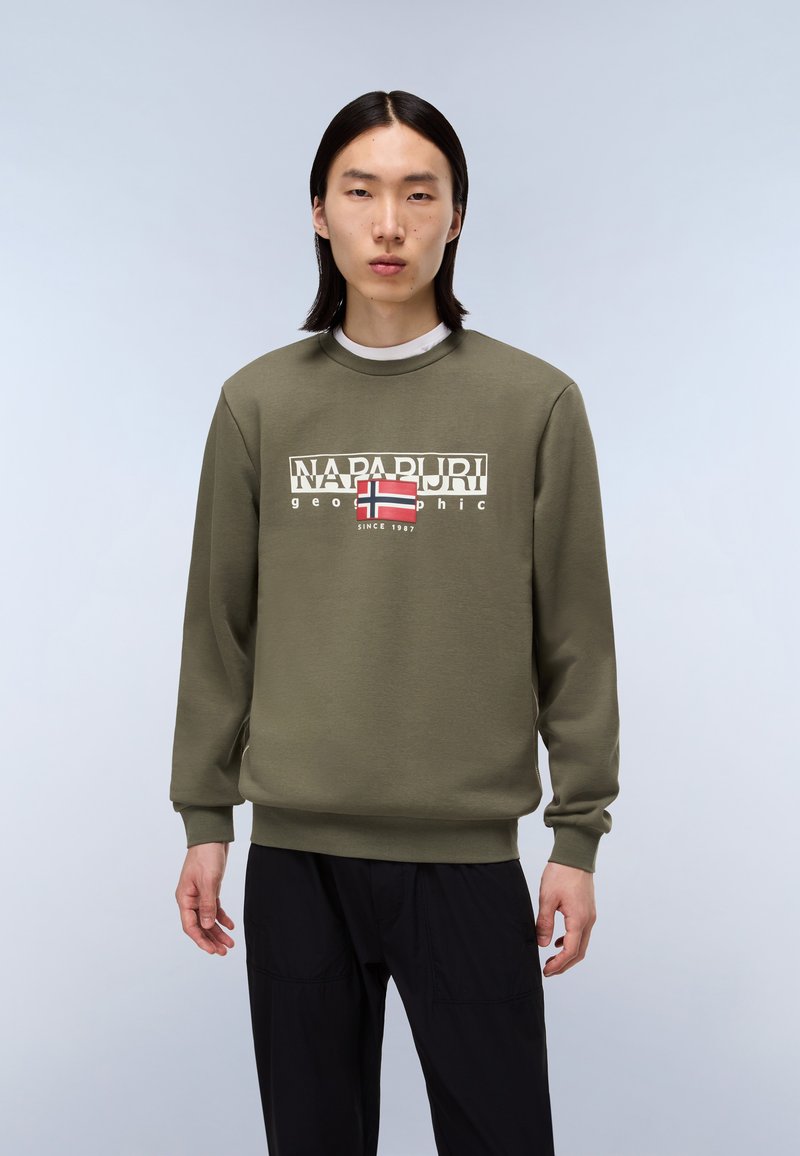 Oliven grøn sweatshirt med rund hals, prydet med et markant grafisk logo i hvid og rød. Lange ærmer og ribbede manchetter. Sorte bukser.