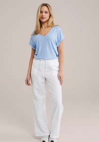 Haut bleu clair à manches courtes en V avec un motif chevron texturé, associé à un pantalon blanc à jambes larges et des baskets blanches.