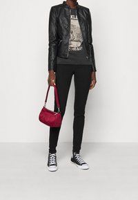 Giacca di pelle nera, T-shirt grafica, jeans skinny neri, sneakers alte nere e una piccola borsa bordeaux con tracolla.