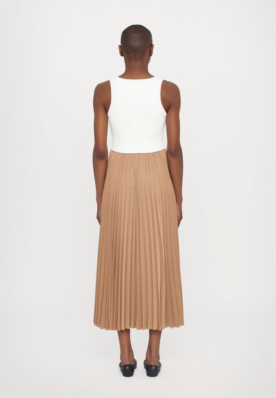 Top a righe bianco abbinato a una gonna midi plissettata beige, che termina sotto il polpaccio, con scarpe nere slip-on. Vista posteriore dell'outfit.
