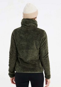 Olijfgroene fleecejack met een hoge kraag en een zachte textuur, gedragen met een lichtbeige gebreide beanie. Geen zichtbare sluitingen of patronen.