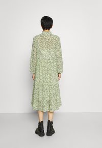 Vihreä kukkakuvioinen midimekko, jossa on laskostettu hame, pitkät hihat ja korkea kaula-aukko. Kuosi sisältää pieniä, hajallaan olevia valkoisia ja tummanvihreitä kukkia.