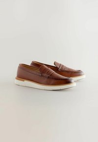 Mocassins en cuir marron avec une semelle en caoutchouc blanc, présentant un accent tissé sur le devant et un design bas pour un enfilage facile.