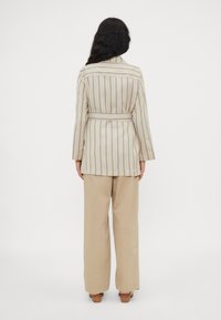 Gestreifte langärmlige Jacke in Beige und Blau, mit einem Gürtel in der Taille; kombiniert mit beigen weit geschnittenen Hosen und Holzabsätzen.