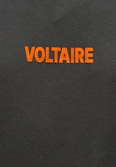 Σκούρο γκρι ύφασμα με έντονα, κεφαλαία πορτοκαλί γράμματα που σχηματίζουν τη λέξη "VOLTAIRE" στο κέντρο της επιφάνειας.