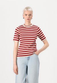 T-shirt a righe rosse e beige con maniche corte, un colletto rotondo a contrasto e una vestibilità comoda, abbinato a jeans in denim azzurri chiari.