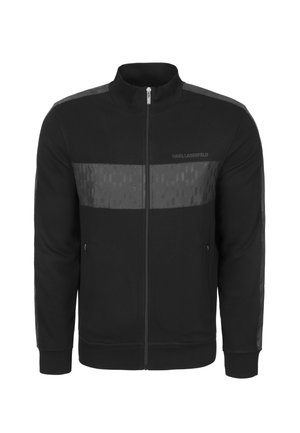 Musta vetoketjullinen collegepaita korkealla kauluksella, jossa on kontrastina matta- ja kiiltävät paneelit sekä hillityt geometriset kuviot edessä ja hihoissa.