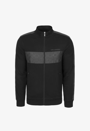 Czarna bluza na zamek z wysokim kołnierzem, z kontrastowymi matowymi i błyszczącymi panelami oraz subtelnymi geometrycznymi wzorami na przodzie i rękawach.