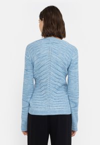 Ljusblå ribbad tröja med en texturerad mönster, långa ärmar och en figurnära design. Observera de vertikala sömmarna och den runda halsringningen.