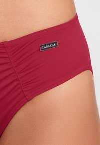 Bikini bottom color lampone con una texture liscia, caratterizzato da un'etichetta in argento con il logo "LASCANA" sul lato e dettagli in tessuto arricciato.