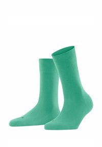 Grüne Baumwollsocken mit glatter Textur, gerippten Bündchen und konischer Form. Sie haben eine minimalistische Markenkennzeichnung an der Unterseite.