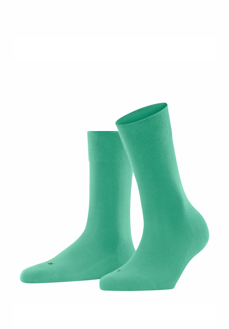 Grüne Baumwollsocken mit glatter Textur, gerippten Bündchen und konischer Form. Sie haben eine minimalistische Markenkennzeichnung an der Unterseite.
