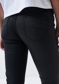 Črne skinny jeans iz raztegljive tkanine, z dvema zadnjima žepoma z okrasnim šivom in gladkim, diskretnim sijajem.
