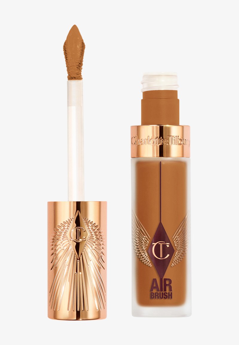 Fond de teint liquide dans un flacon en verre avec un bouchon doré et un logo ailé, accompagné d'un applicateur crème. Les deux dans une teinte marron chaud.