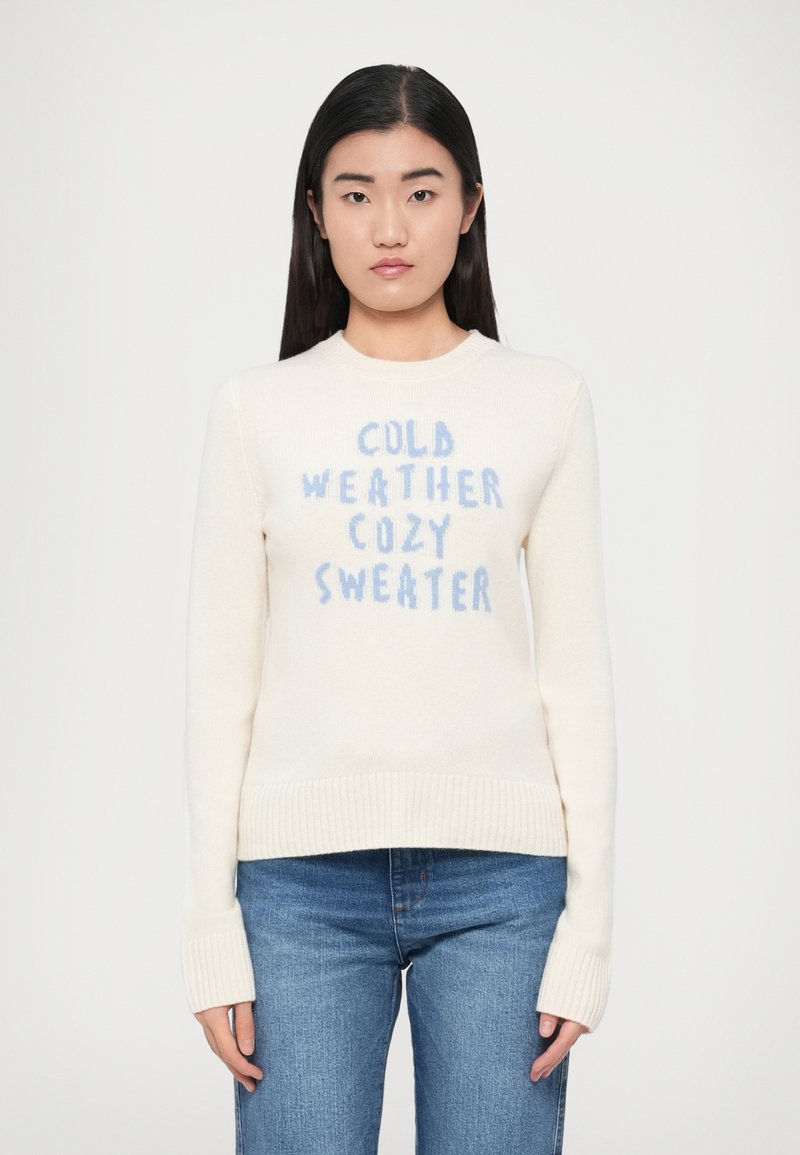 Kreemikas kampsun soonikkoes äärega allosas ja varrukaotstes. Sinise tekstiga, mis ütleb "KÜLMAS ILMAS SOE KAMPSUN." Pehme tekstuur, pikad varrukad.