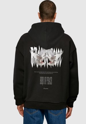 Černá oversized mikina s kapucí, na zadní straně s grafikou dvou bílých holubic, nad nimiž je text a zubatý designový prvek.