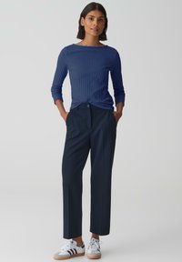 Navy ribbed long-sleeve top with a boat neckline, paired with tailored dark pants and white sneakers featuring black stripes.